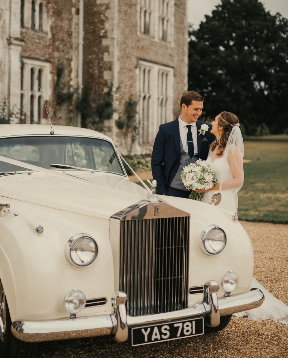 Et brudepar står ved siden af en Rolls Royce foran et slot.