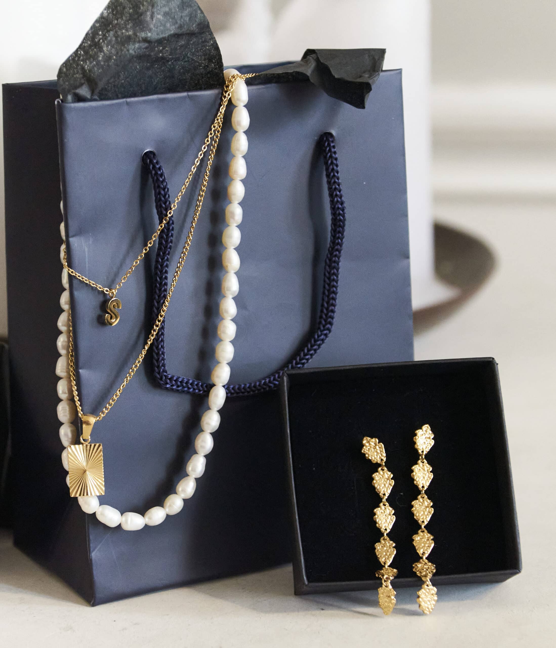 En gavepose med en halskæde, øreringe og perler.