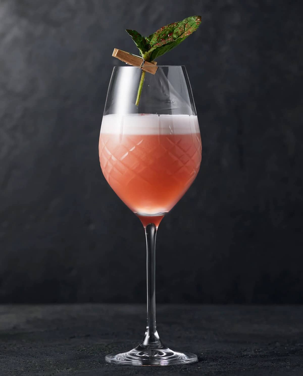 Rød cocktail med en klemme, der holder et mynteblad.